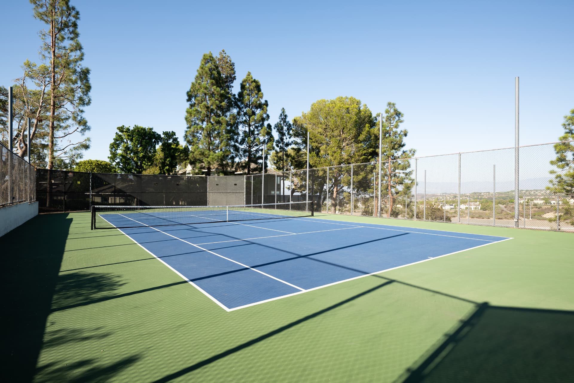 Community tennis court surrounded by trees with coastal views beyond