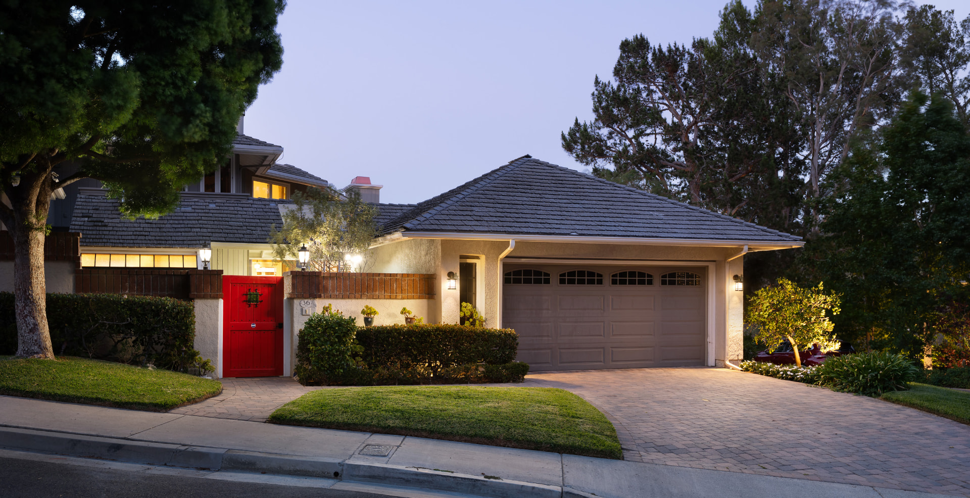 Twilight view of 36 Vienna with the lighted red front gate and manicured landscaping